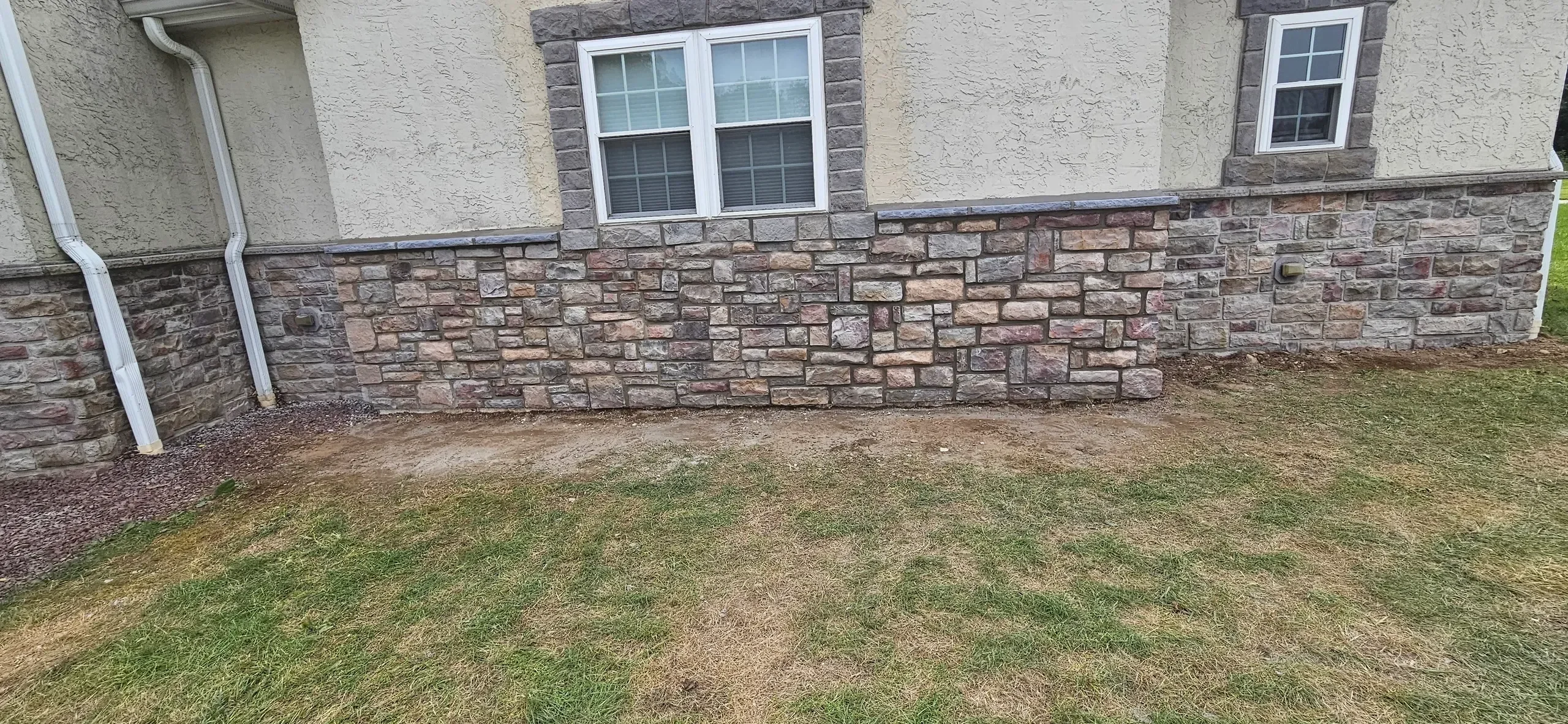 Completed stone veneer meets stucco siding below bright windows.